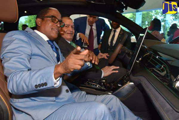 Minister of Transport and Mining, Audley Shaw (second left), sits at the wheel of one of the Build Your Dreams (BYD) electric vehicles. Seated at left is State Minister in the Ministry of Industry, Investment and Commerce (MIIC), Dr. Norman Dunn. Observing (at third left) is investor in the EV distributing company, Flash Motors, Zachary Harding. Photo credit: Mark Bell/JIS.